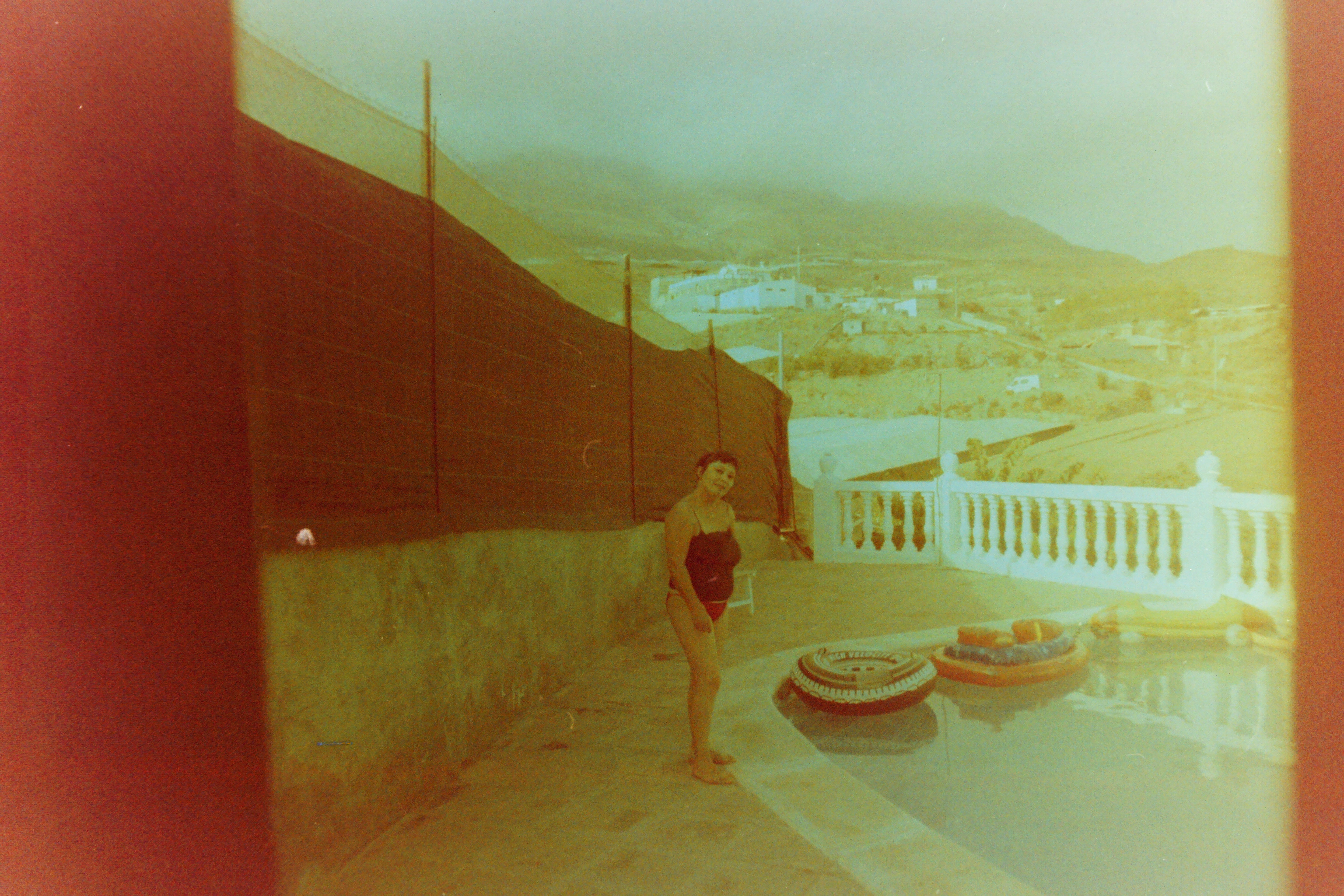 Niña junto a una piscina con paisaje al fondo fotografiada en un carrete caducado
